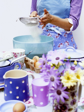 Woman Sieving Flour into a Bowl, Crockery & Eggs in Front