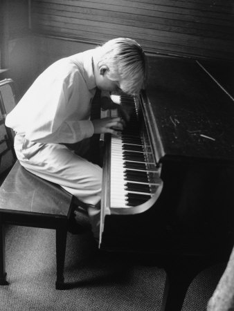 black and white photograph of boy about six playing grand piano