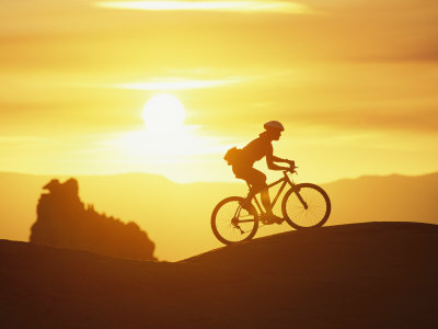 Buy A Woman Rides Her Bike in the Sunset with Rock Cliffs in the Background at AllPosters.com