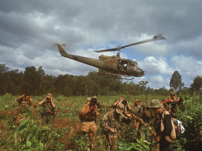 American UH1 Huey Helicopter Lifting Off as Personnel on the Ground Protect Themselves Poster