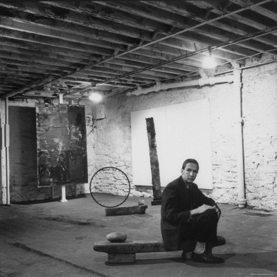Robert Rauschenberg Sitting on His Sculpture in Studio, Among Other Paintings and Sculptures