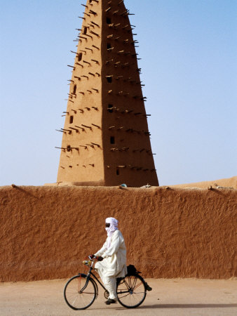 Buy Robed Tuareg Man Cycling Past Minaret of Mud-Brick Grande Mosquee, Agadez, Niger at AllPosters.com
