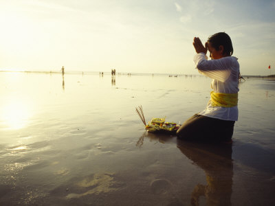 A Kneeling Hindu Balinese Woman Prays and Gives Offerings at Sunset