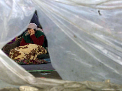An Elderly Kosovar Woman Sits Behind a Plastic Wind Guard Around Her Spot