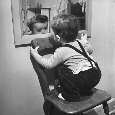 Little Boy Standing on Chair to See Face in Mirror
