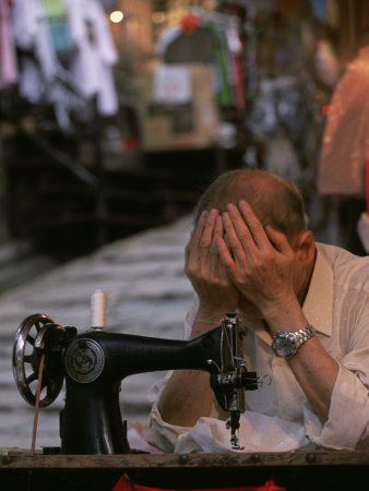 Tailor Puts His Head in His Hands in Front of His Sewing Machine