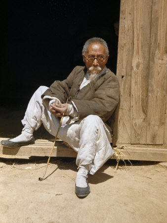 Man Holding Pipe and Wearing Traditional Clothing Sits in Doorway