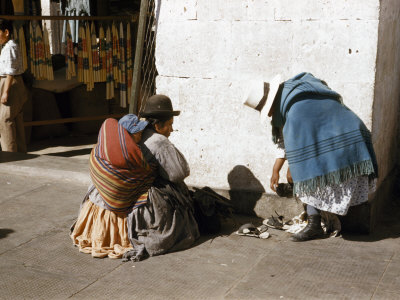Woman Removes Shoes to Try on Sandals Sold by Vendor Carrying Infant