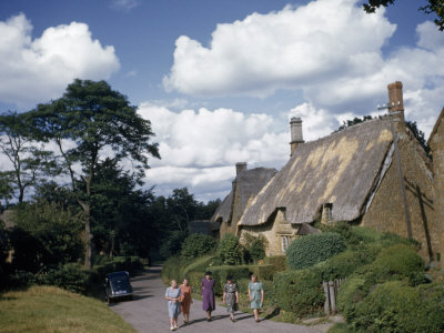 Women Stroll Down a Country Lane Past Thatched Roof Cottages