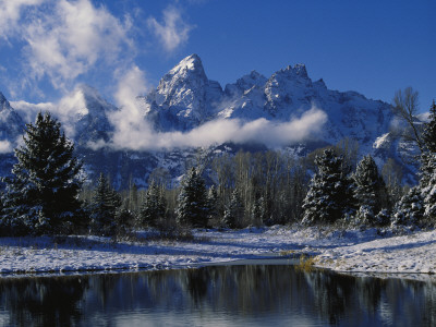 Winter Scene of Clouds Drifting across Snowy Mountain Peaks Above Pine Trees Is Reflected in Water