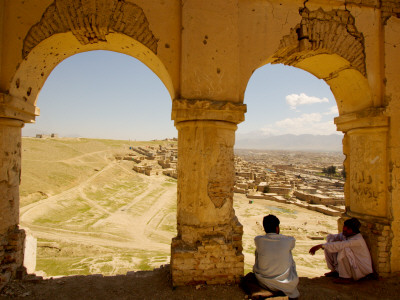 Locals Chat under Arches of Old Tomb with City in Background.