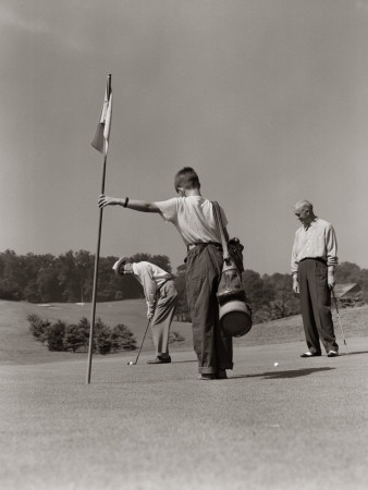 Golfer Getting Ready To Putt With Boy Caddy Holding Flag and Partner Looking on From Side Poster