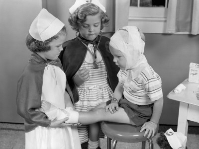 Two Young Girls Dressed As Nurses, Bandaging Three Year Old Boy