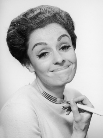 A Woman With a Whimsical Expression Holds Up a Fork, Circa 1960