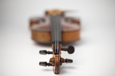 A violin lies on a flat white surface; the photo is taken from the scroll of the violin, everything beyond the scroll is out of focus.