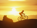 Buy A Woman Rides Her Bike in the Sunset with Rock Cliffs in the Background at AllPosters.com