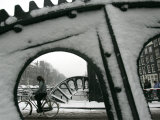 A Cyclist Passes a Draw Bridge as Snow Covers the City Center of Amsterdam