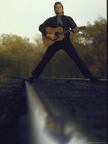 Country/Western Singer Johnny Cash with Guitar Straddling Railroad Tracks