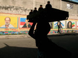 A Boy Carrying Bottles on His Head Passes by a Wall with Pictures of Haitian President Renel Preval