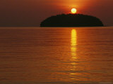 Buy The Sun Casts a Red Glow and a Reflection as It Sets Behind an Island at AllPosters.com