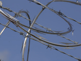 Close-up of Coiled Razor Wire and Barbed Wire on a Fence Against Blue Sky