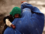 An Afghan Woman Holding Her Child Throws Back Her Burqa to See Her Way Along a Muddy Alley