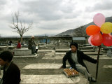 An Afghan Boy Sits on a Grave Plot and Sells Balloons and Eggs as Others Relax