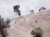 People Walking up a Path on a Hillside Towards a Hut in Rural Haiti