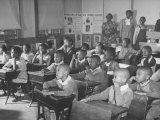 Children Sitting at their Desks in a Classroom, Teachers at the Rear of the Room