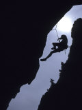 Silhouette of Rock Climber Hanging from Cliff Face