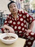 Man in Silk Pajamas Eats a Bowl of Noodles on the Street