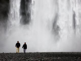 Two People Walking Near a Large Waterfall
