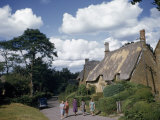 Women Stroll Down a Country Lane Past Thatched Roof Cottages
