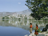 Buy Women Stand Beside Mirror-Like Lake Reflecting Nearby Town at AllPosters.com