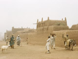 Buy Pedestrians Robed Against Dusty Wind Walk Past Mud Houses at AllPosters.com