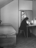 Nun Sitting at Small Table and Writing in Corner of Her Room