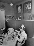 Buy Nurse Sitting at Table with Medical Supplies While Doctors Examine Patient in Background at AllPosters.com
