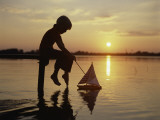 Silhouette of Boy Sitting at Pier with Toy Sailboat