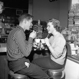 Teen Couple on Stools at Soda Fountain Drinking Shakes and Smiling at Each Other