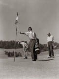 Golfer Getting Ready To Putt With Boy Caddy Holding Flag and Partner Looking on From Side