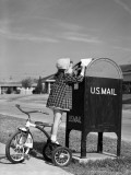 Girl Standing on Tricycle on Suburban Sidewalk, Mailing Letter in Mailbox