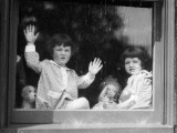 Two Frowning Girls With Dolls Looking Out Large Window at Rain Drops