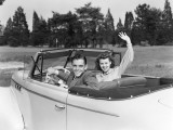 Teenage Couple in Convertible Car Smile and Wave To Viewer