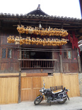 A Motorcycle Parked under Corn Cobs Hanging from Eaves to Dry