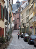 A Woman Rides a Bike Up a Cobbled Street in the Morning