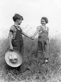1930s 1940s Boy Girl Holding Hands Walk Down Grassy Hill Wearing Overalls Carrying Straw Hat
