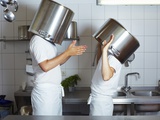Two Chefs Having Discussion with Large Pans on their Heads