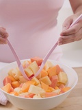 Woman Taking Fruit Salad Out of Bowl with Salad Servers
