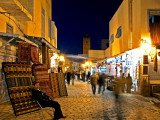 People Strolling along Cobblestone Street Past Carpet Seller at Twilight  Kairouan  Tunisia