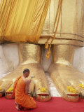 Buddhist Monk Kneeling in Prayer at the Feet of a Statue of the Standing Buddha  Thailand